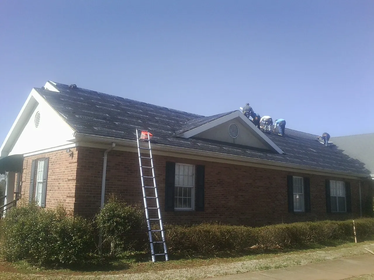 Crew tearing shingles off a brick ranch roof with a ladder set — Emergency Roof Repair work by our crew in Eastham