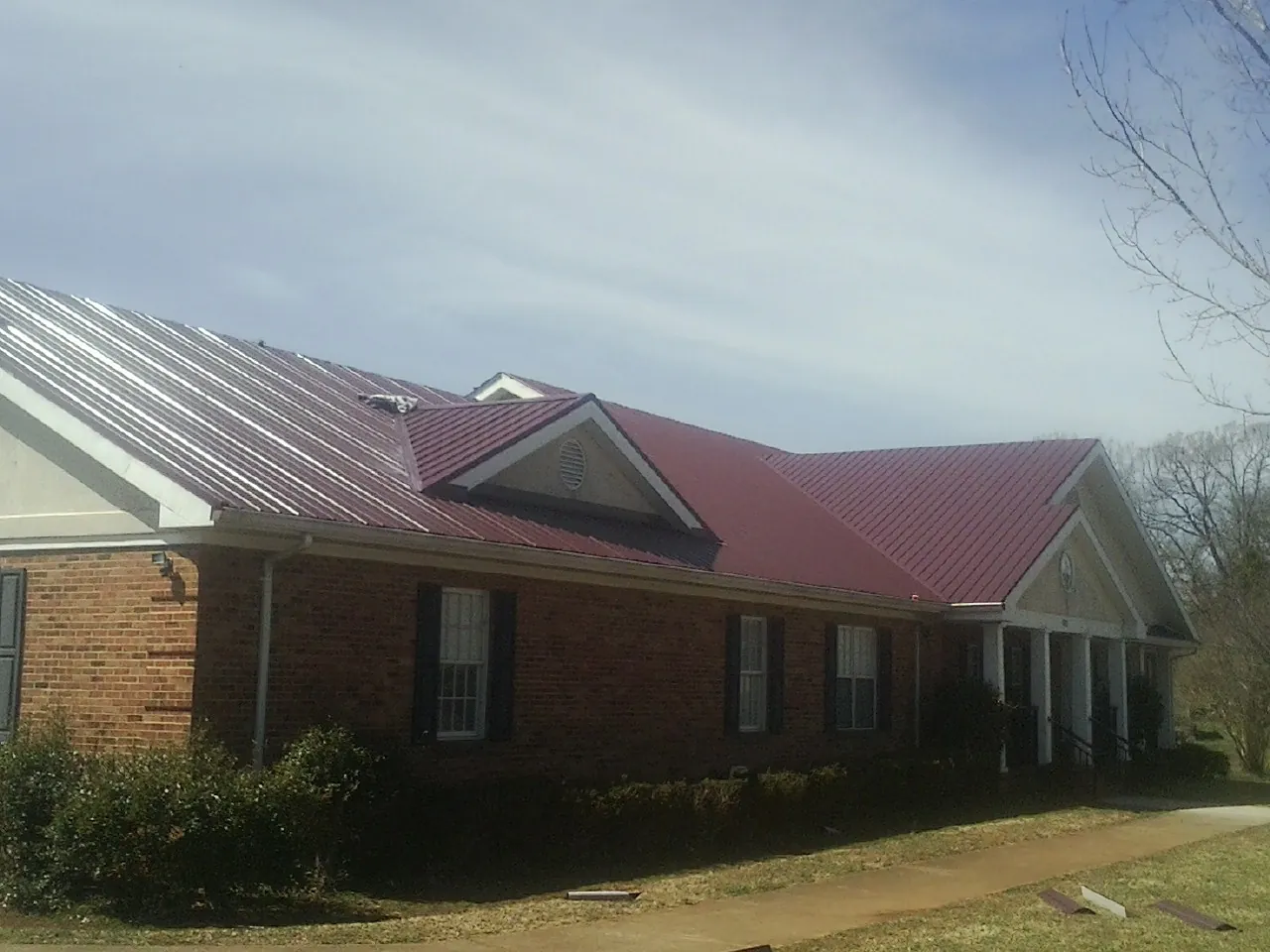 Red metal roof with gabled entries on a long brick building, from a Hail Damage Roof Repair job in Eastham
