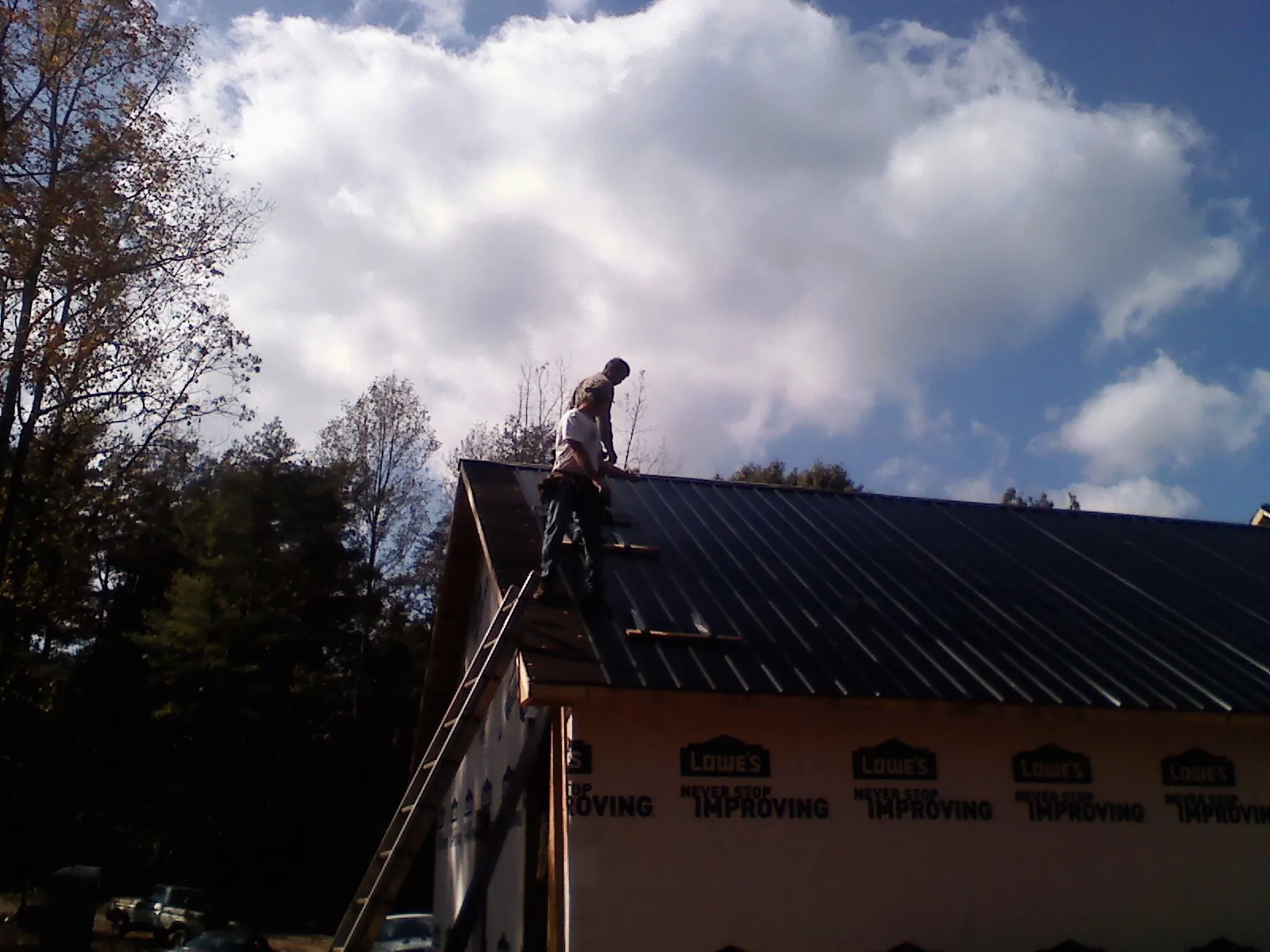 Roofer fastening dark metal panels high against a cloudy sky, from a Roof Inspection job in Eastham